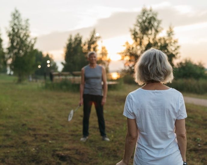 Elderly couple playing badminton outdoors at sunset, enjoying leisure time together.