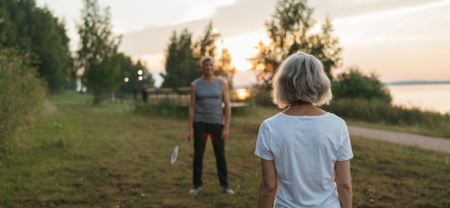 Elderly couple playing badminton outdoors at sunset, enjoying leisure time together.