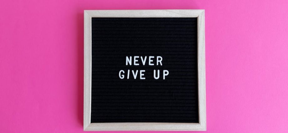 A framed letter board with 'NEVER GIVE UP' on a vibrant pink background.